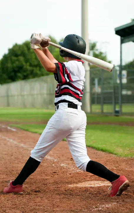 A young baseball player swings a bat, wearing a black helmet, a red and white jersey, and black pants on a field